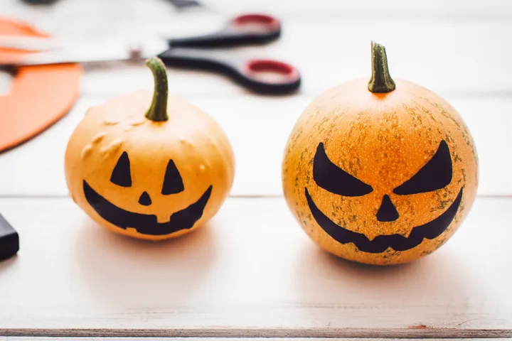 Two small pumpkins of different sizes with black faces stand side by side.