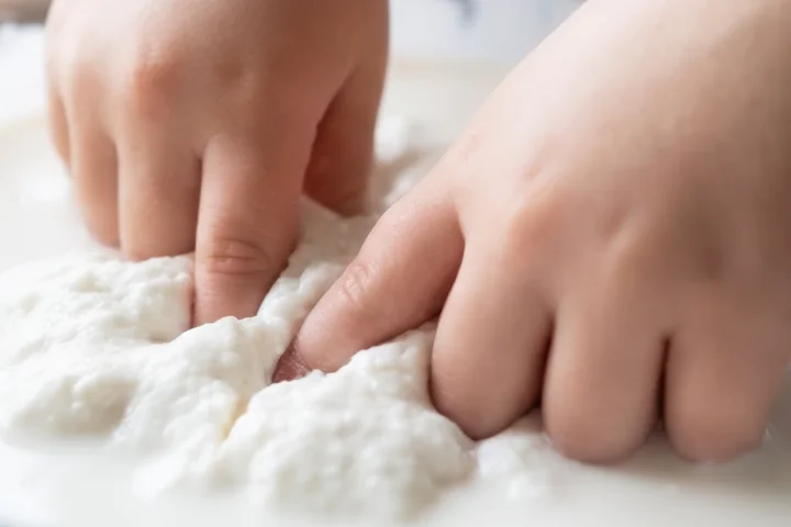 Child's hands pressing into a white cornstarch mixture.
