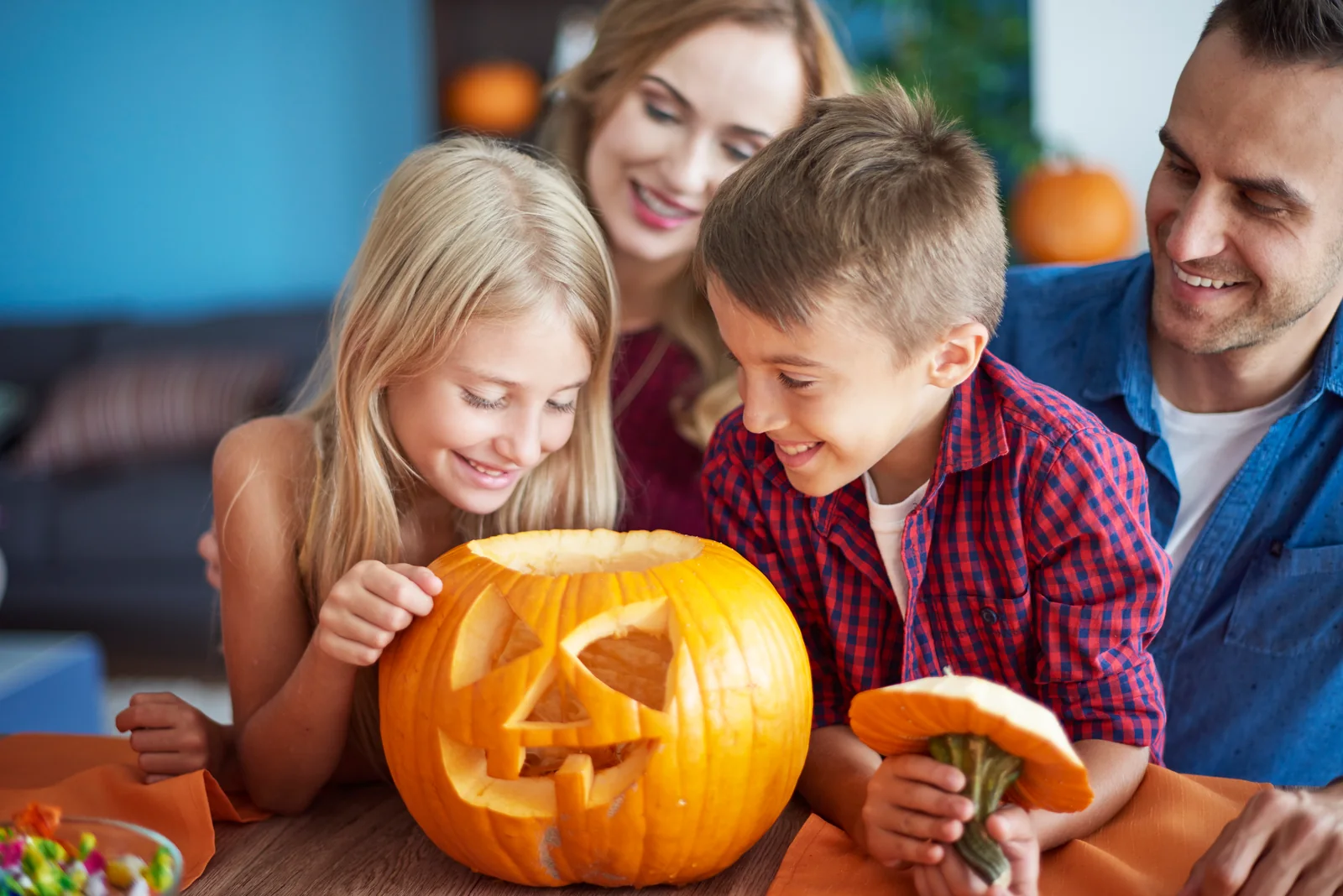 Family Halloween pumpkin activity Parents and two children smile at a carved pumpkin on a table.